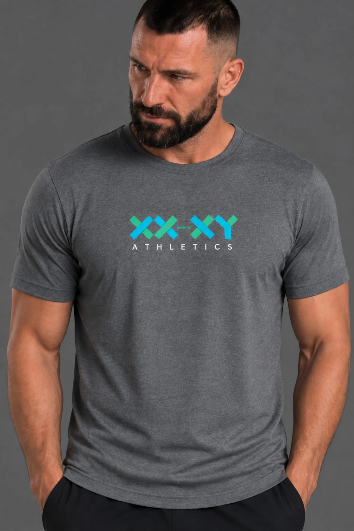 A muscular man wearing a dark heather gray t-shirt with a 'XX-XY ATHLETICS' graphic in teal and white on the chest, posed against a solid gray background.