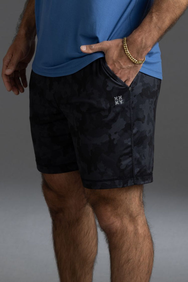 Person wearing black camouflage shorts and a blue shirt on a gray background || Black Camo