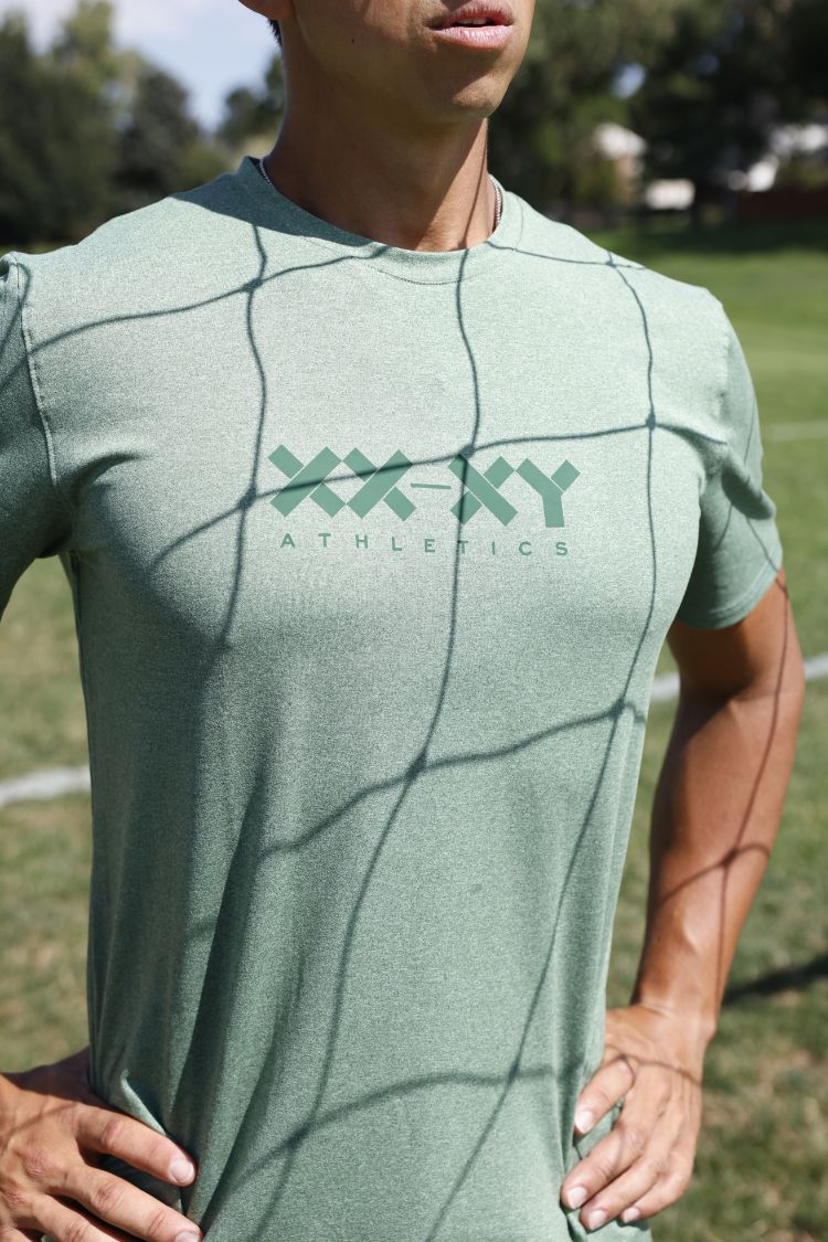 Person wearing a green athletic t-shirt with 'XXY Athletics' logo on a grassy field.