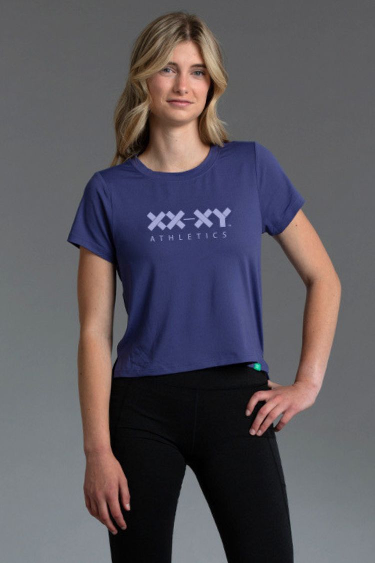 Woman wearing a blue 'XXXY Athletics' t-shirt on a gray background