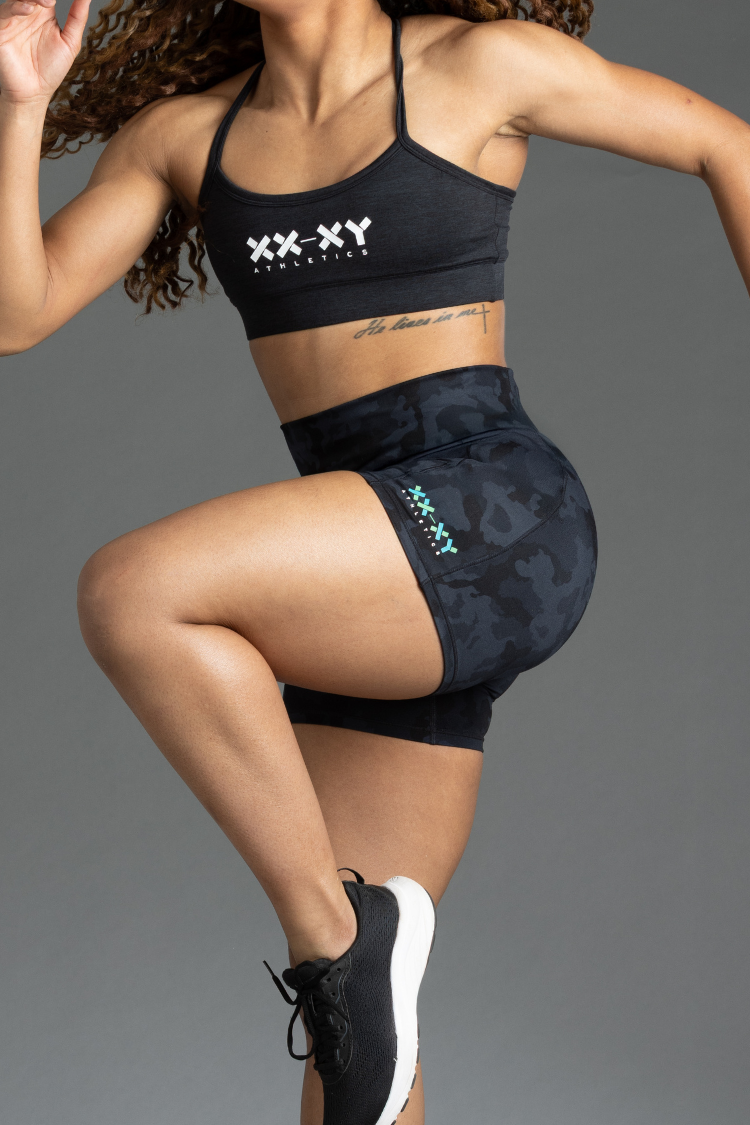 Person wearing black sports bra and shorts with visible branding on a gray background