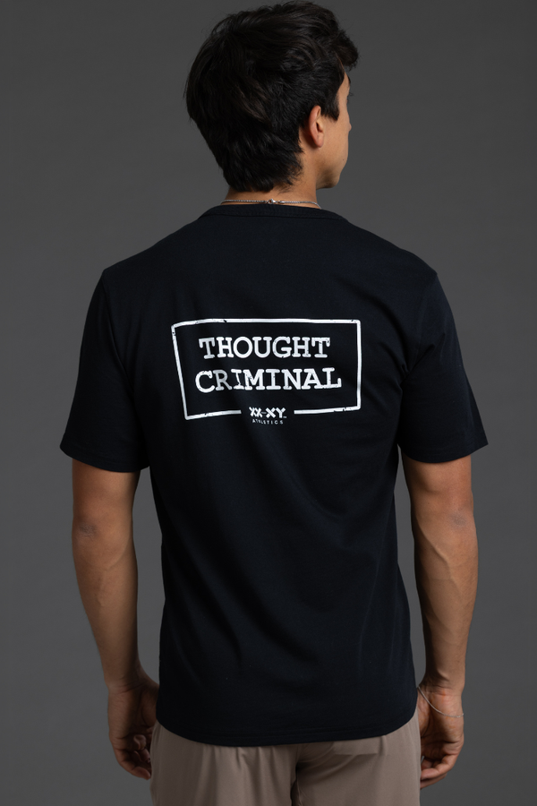 Person wearing a black t-shirt with 'THOUGHT CRIMINAL' text on the back against a gray background || Black