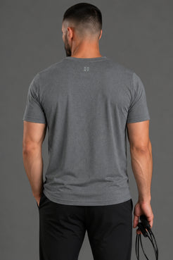 Man wearing a gray t-shirt with a small logo on the back against a gray background || Dark Heather Gray