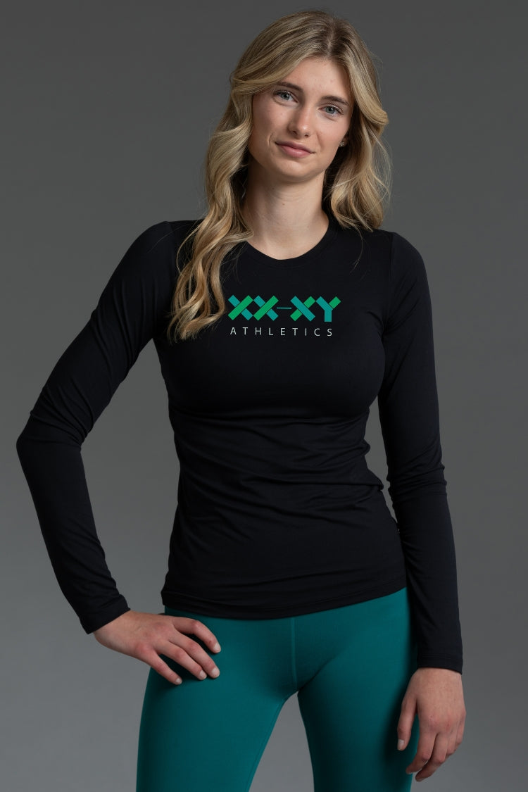 Woman wearing a black long-sleeve shirt with 'XXXY Athletics' logo and teal leggings on a gray background