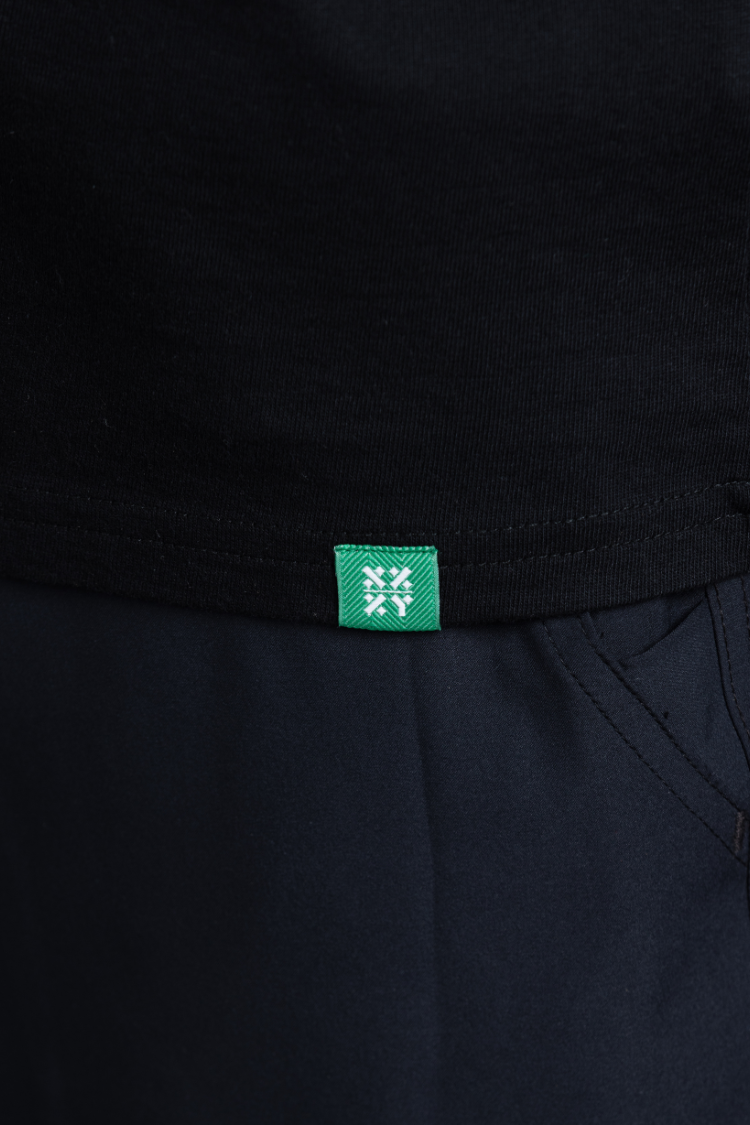 Close-up of a black garment with a green label featuring a white logo. || Black