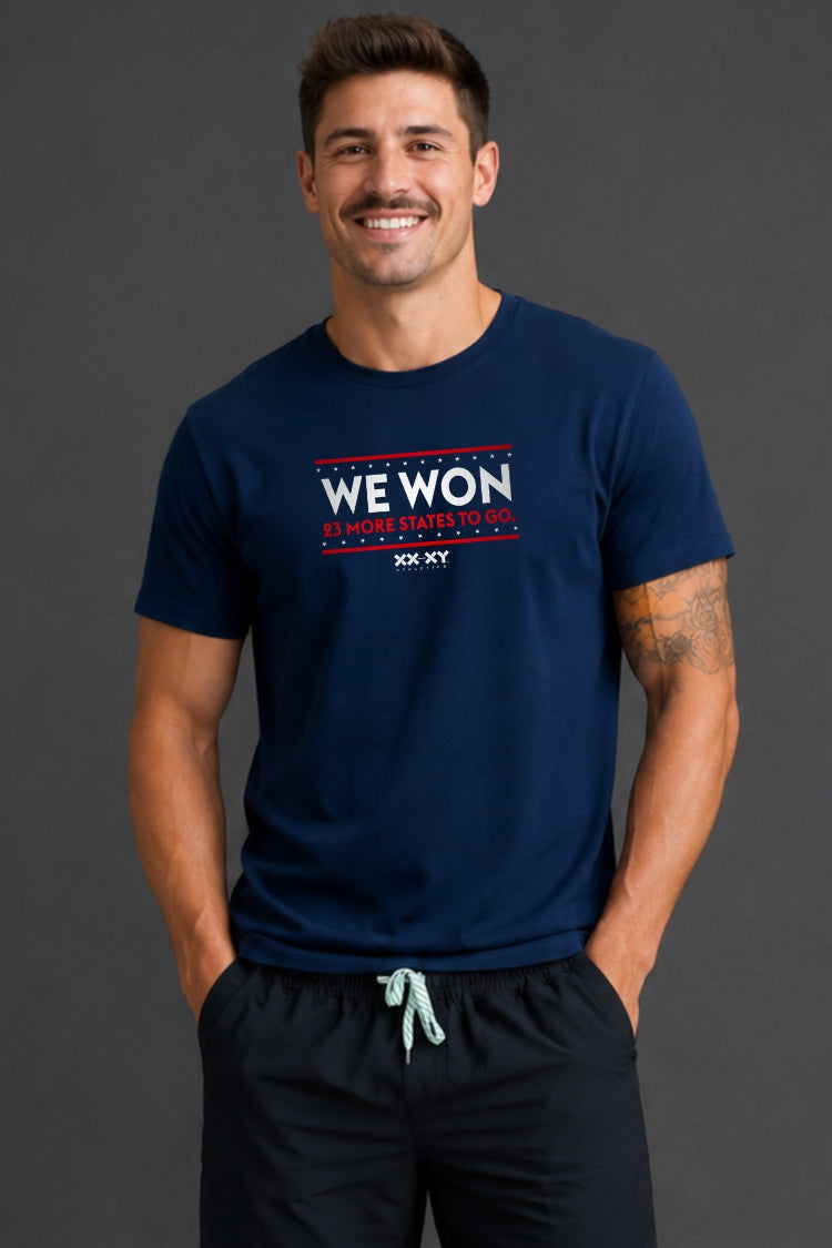 Man standing in front of gray background wearing a navy tshirt with WE WON text on it.