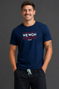 Man standing in front of gray background wearing a navy tshirt with WE WON text on it. || Navy