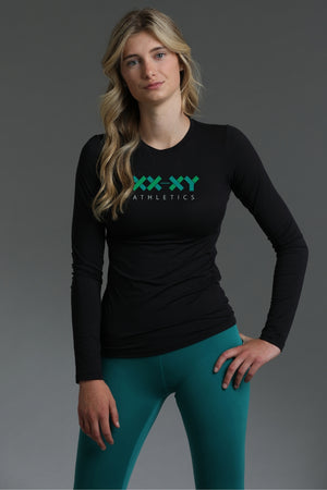 Woman wearing a black long-sleeve shirt with 'XXY Athletics' logo and teal leggings on a gray background || Black
