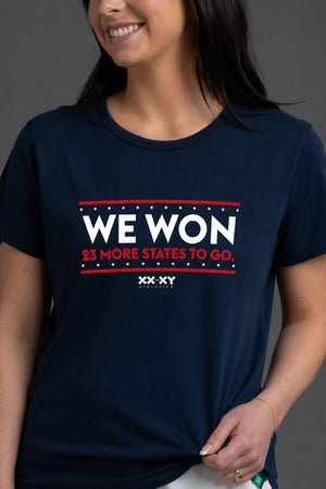 Person wearing a navy blue t-shirt with 'WE WON 23 MORE STATES TO GO' text on a gray background || Navy