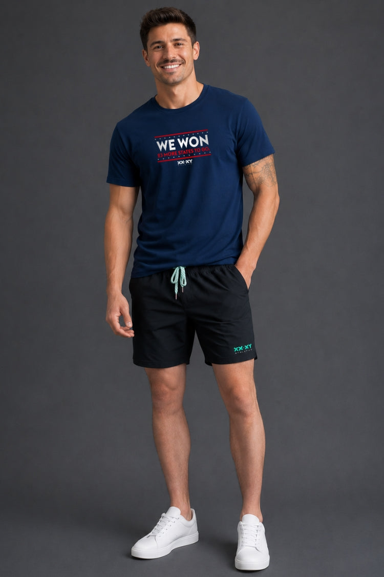 Man standing in front of gray background wearing a navy tshirt with WE WON text on it. || Navy