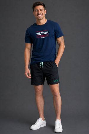 Man standing in front of gray background wearing a navy tshirt with WE WON text on it. || Navy