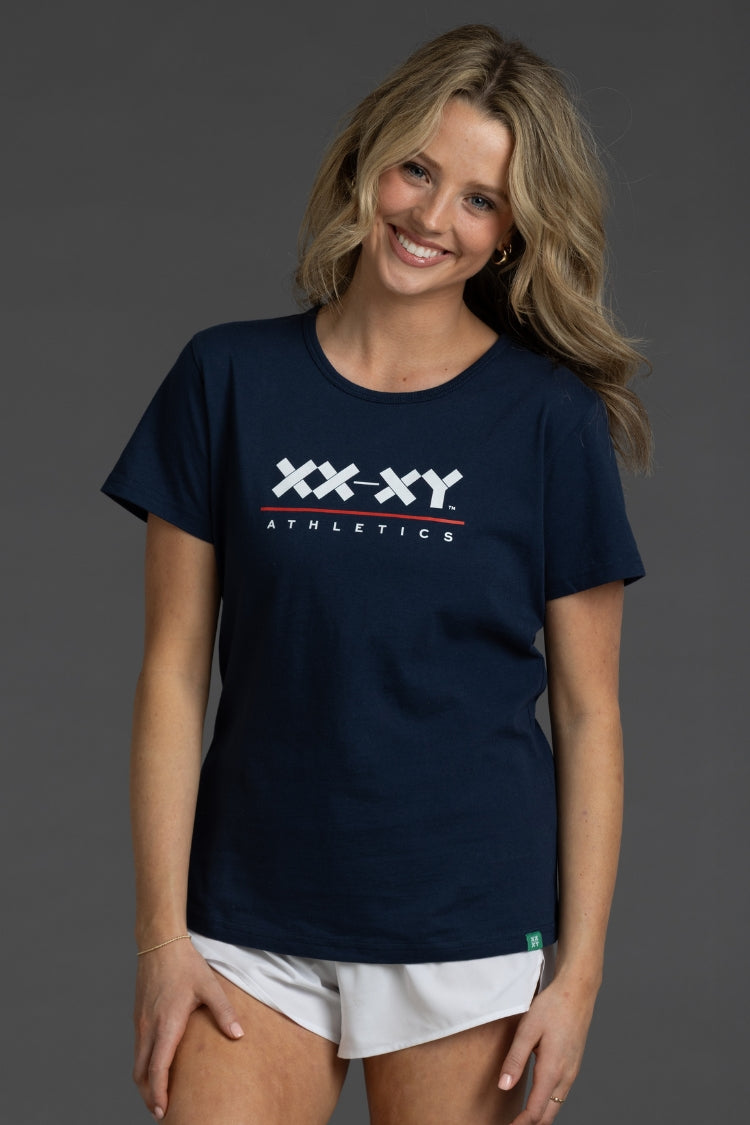 Woman wearing a navy blue t-shirt with 'XXXY Athletics' logo on a gray background || Navy
