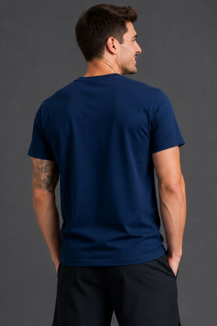 Man standing in front of gray background facing backwards and wearing a navy tshirt.