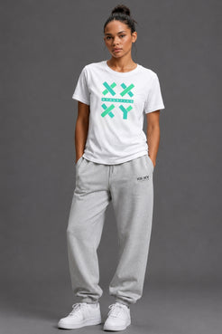 A woman modeling a white crewneck t-shirt with a green XXYY graphic and light gray sweatpants, standing against a solid gray studio background. || White