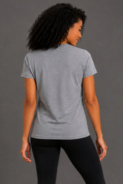 A woman with curly black hair is shown from the back wearing a heather gray short-sleeve t-shirt and black leggings against a solid gray studio background. || Heather Gray
