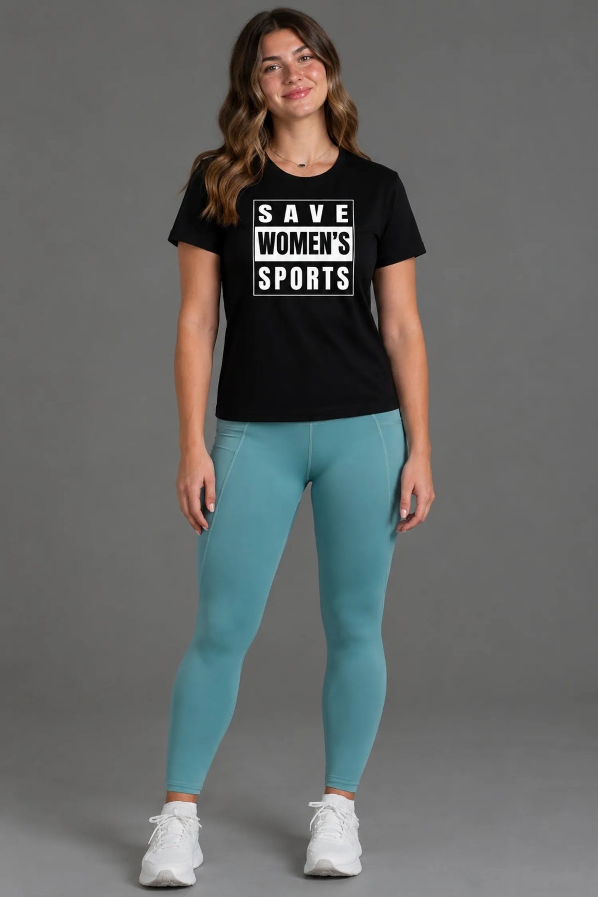 Female model wearing a black Save Women’s Sports graphic tee with teal leggings and white sneakers.