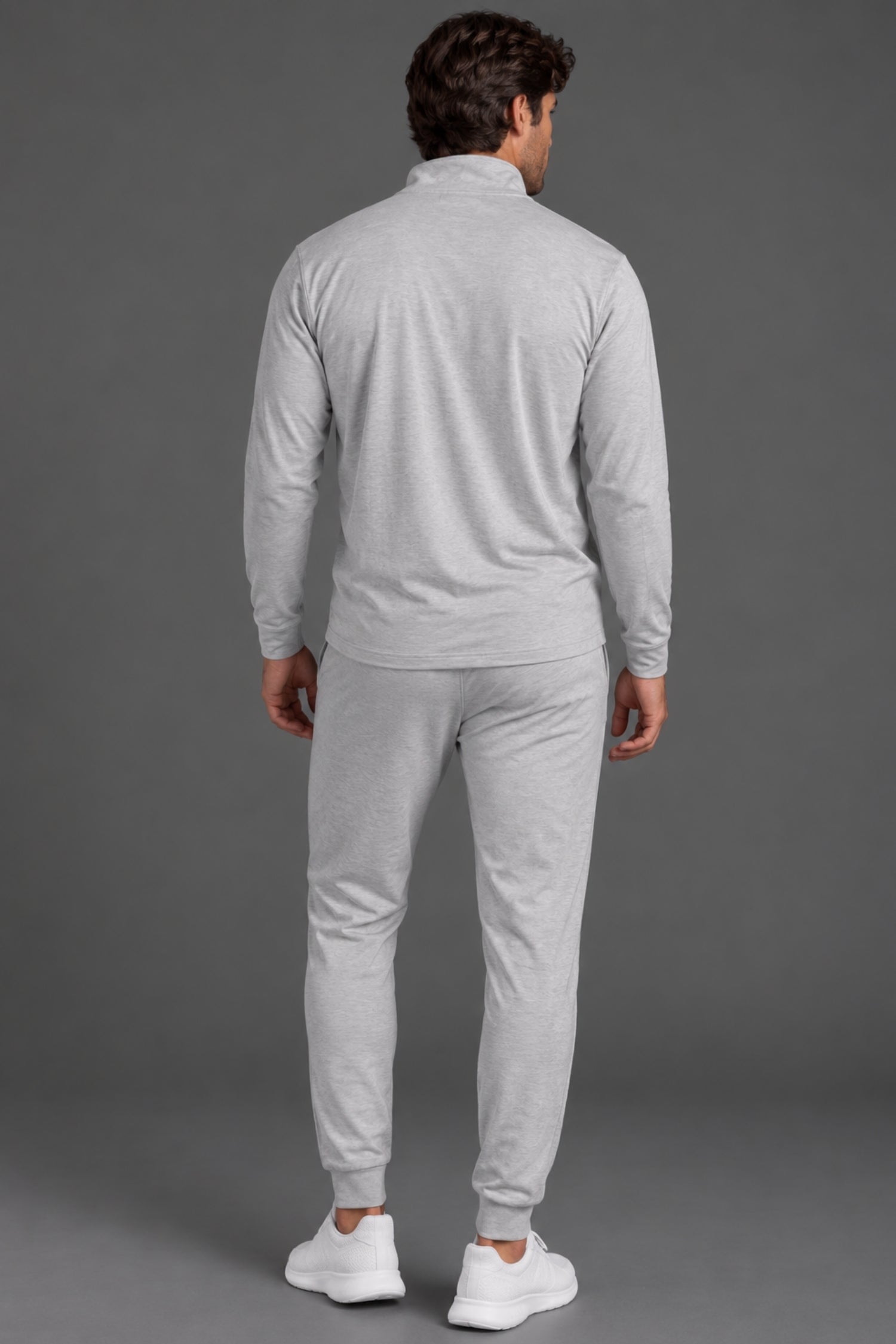 Back view of a male model wearing a light gray quarter-zip pullover with matching gray joggers and white sneakers against a gray studio background. || Light Heather Gray - 1