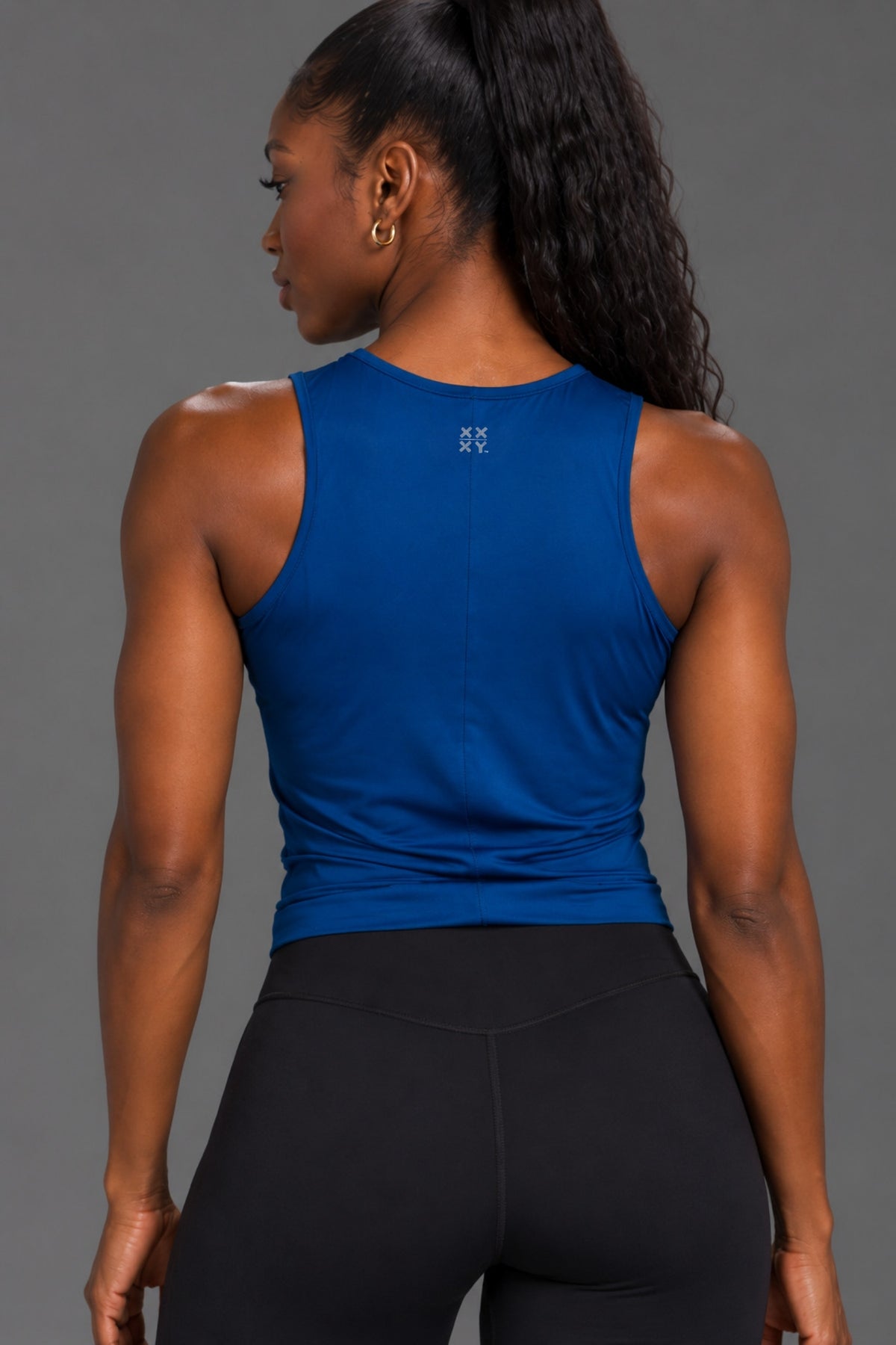 Close-up back view of Black female model wearing a blue tank with XX-XY Athletics logo at the upper back.