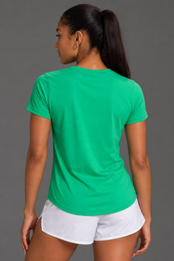 A woman shown from the back wearing a bright green short-sleeve athletic T-shirt and white shorts against a plain gray studio background. || Kelly Green