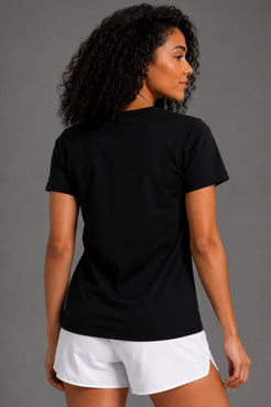 A woman with curly black hair is shown from the back wearing a plain black short-sleeve t-shirt and white athletic shorts against a solid gray studio background. || Black