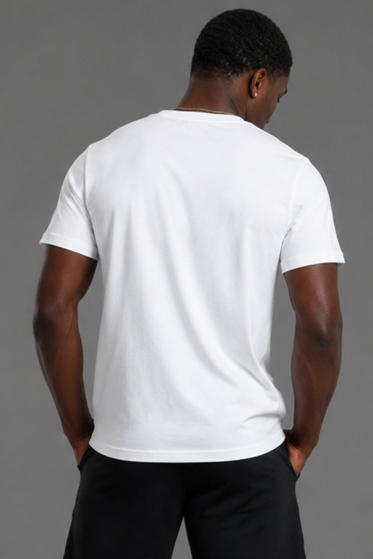 A man viewed from behind wearing a plain white short-sleeve crew-neck t-shirt and black pants, standing against a solid gray studio background.