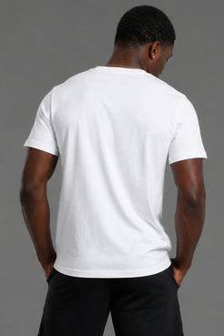 A man viewed from behind wearing a plain white short-sleeve crew-neck t-shirt and black pants, standing against a solid gray studio background. || White