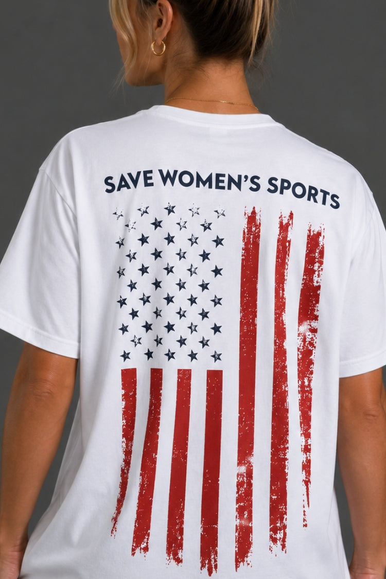 A woman shown from the back wearing a white t-shirt with a distressed American flag graphic and the text 'SAVE WOMEN'S SPORTS' printed in black across the upper back.