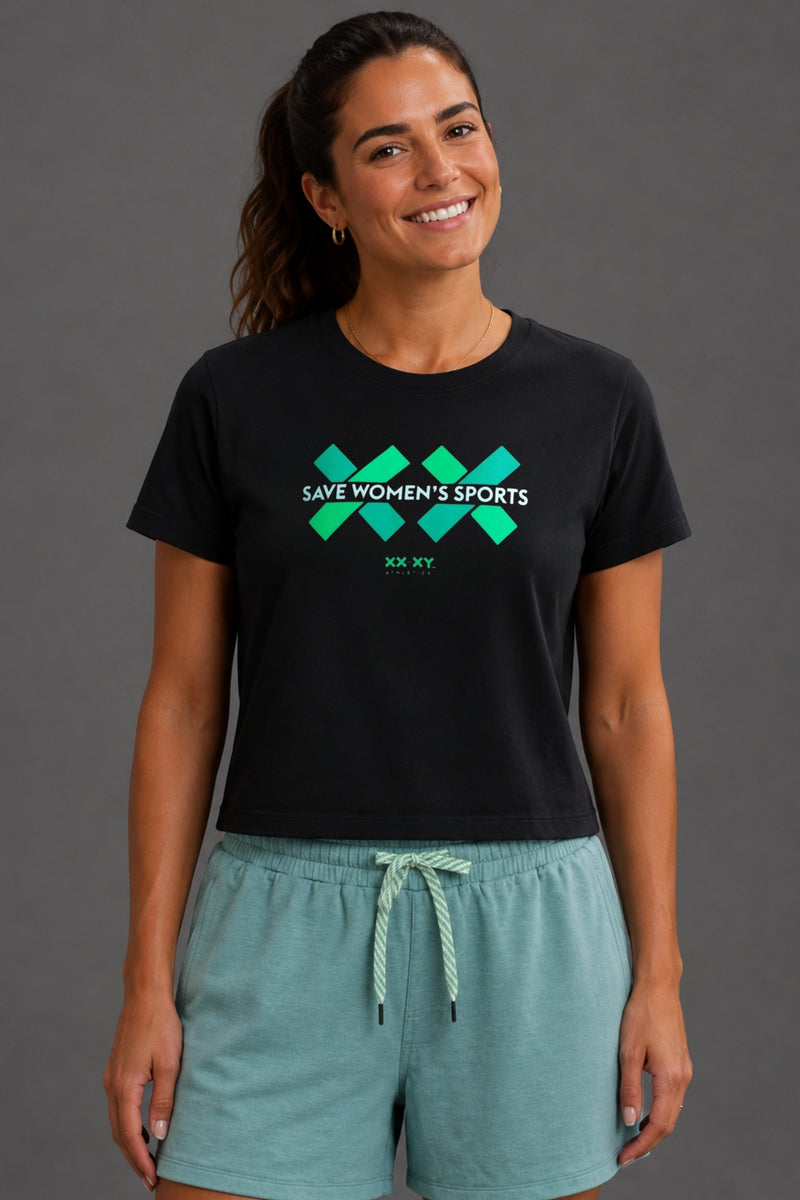 Woman wearing a black t-shirt with a green and teal graphic and blue shorts on a gray background. || black