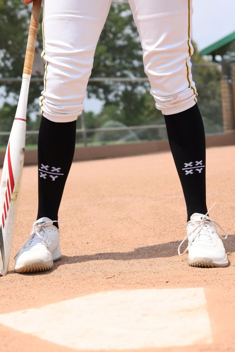Baseball player on a field wearing black socks with white logo and white shoes.
