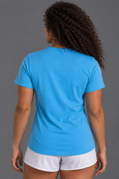A woman viewed from behind wearing a bright blue short-sleeve t-shirt and white athletic shorts against a solid gray studio background. || Light Blue