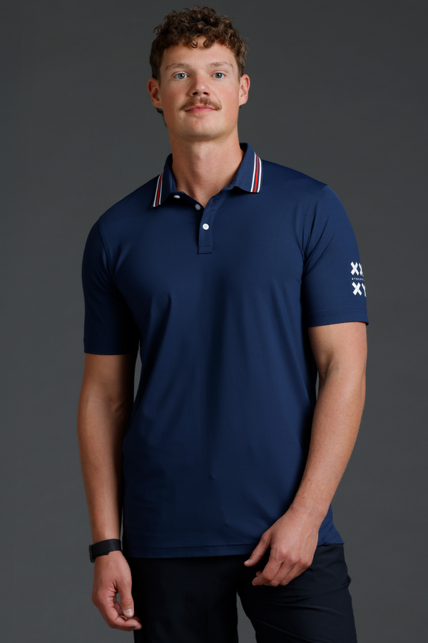 Man wearing a navy blue polo shirt with a logo on a gray background || Navy