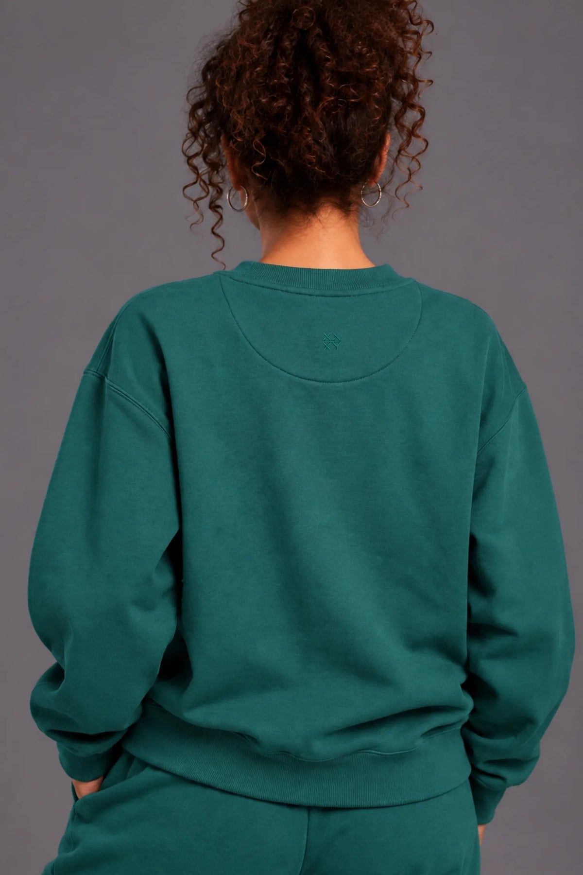 Back view of a teal XX-XY Athletics crewneck sweatshirt with a subtle embroidered logo below the neckline.