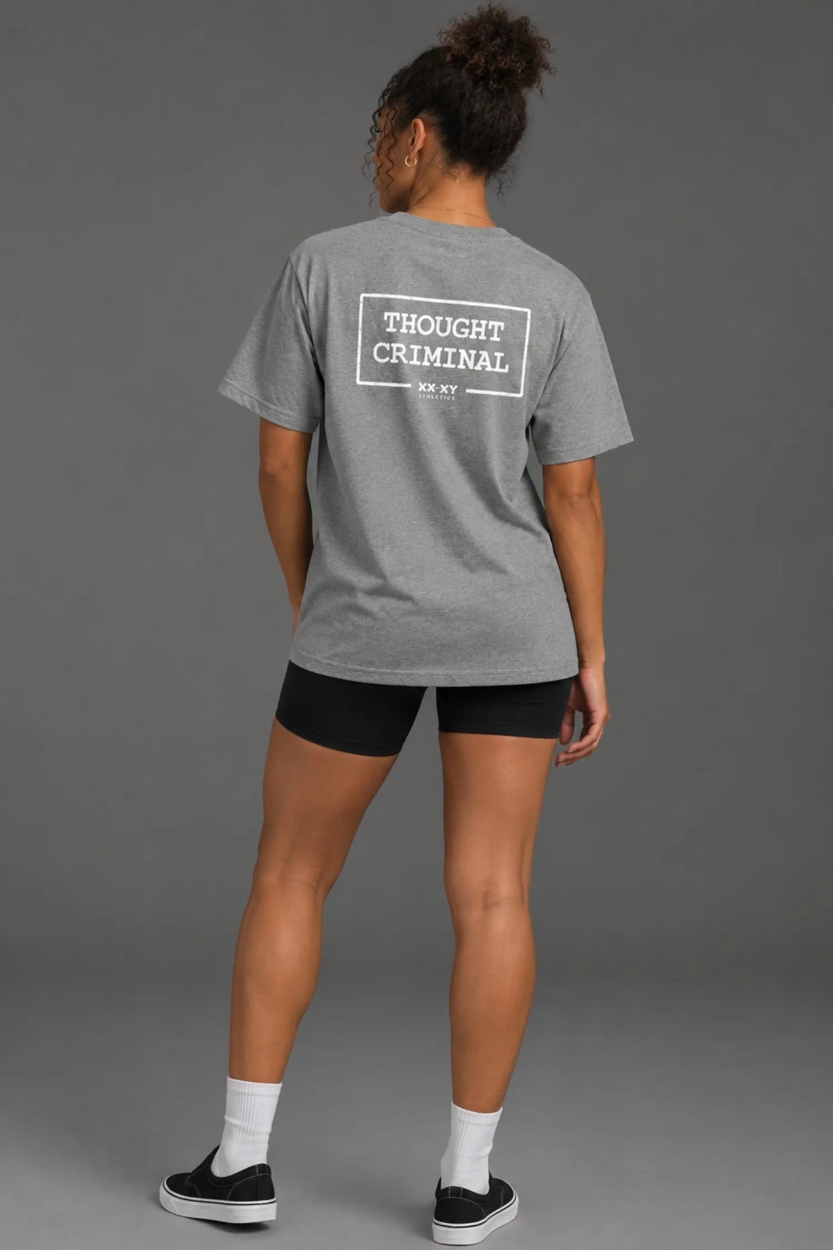 Black female model wearing a boyfriend-fit gray Thought Criminal graphic tee with black bike shorts.