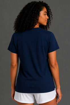 A woman with curly black hair wearing a navy blue short-sleeve t-shirt paired with white shorts, against a gray studio background. || Dark Navy