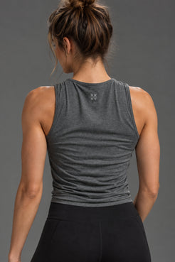 Rear view of a woman wearing a dark heather gray sleeveless athletic tank top and black leggings against a solid gray studio background. || Dark Heather Gray