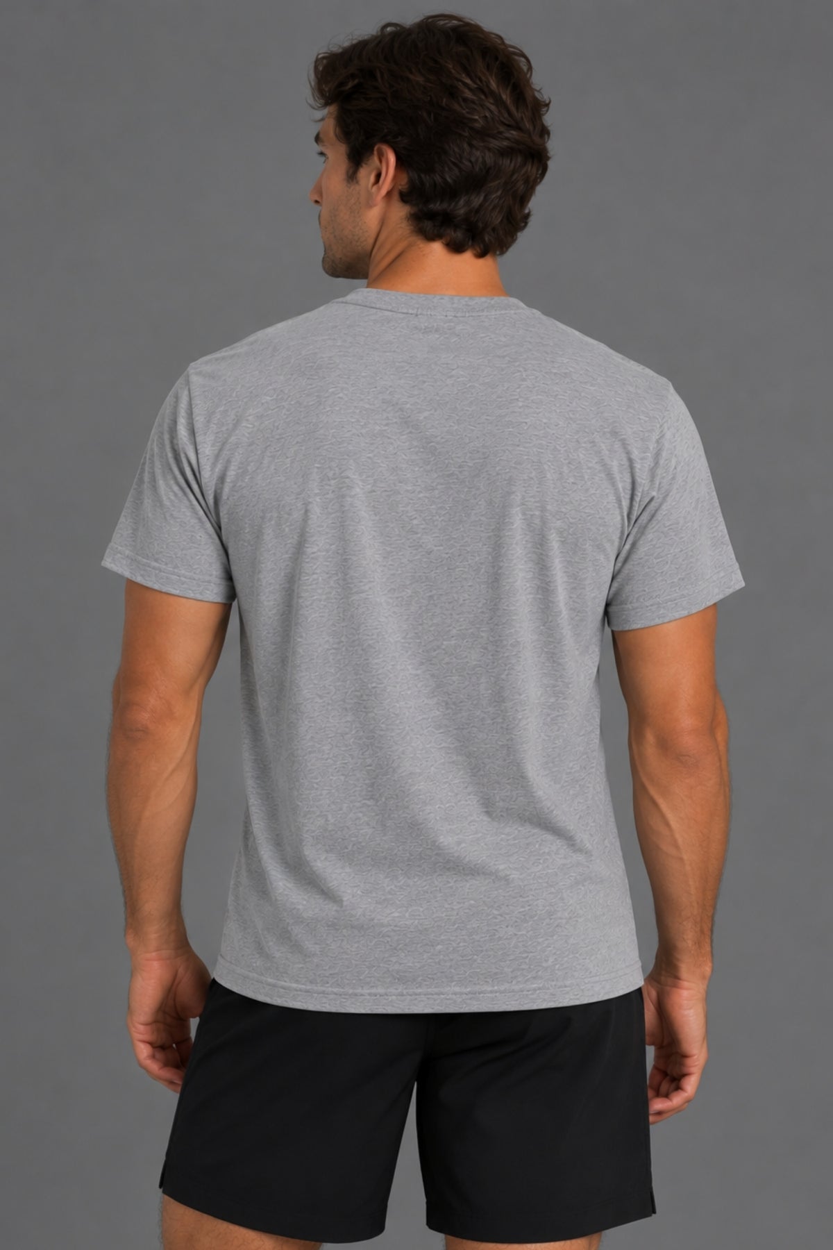 Back view of male model wearing a plain gray T-shirt with black athletic shorts against a gray background.