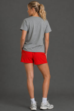A woman shown from the back wearing a heather gray t-shirt, bright red athletic shorts, white socks, and gray running shoes against a solid dark gray studio background. || Light Heather Gray