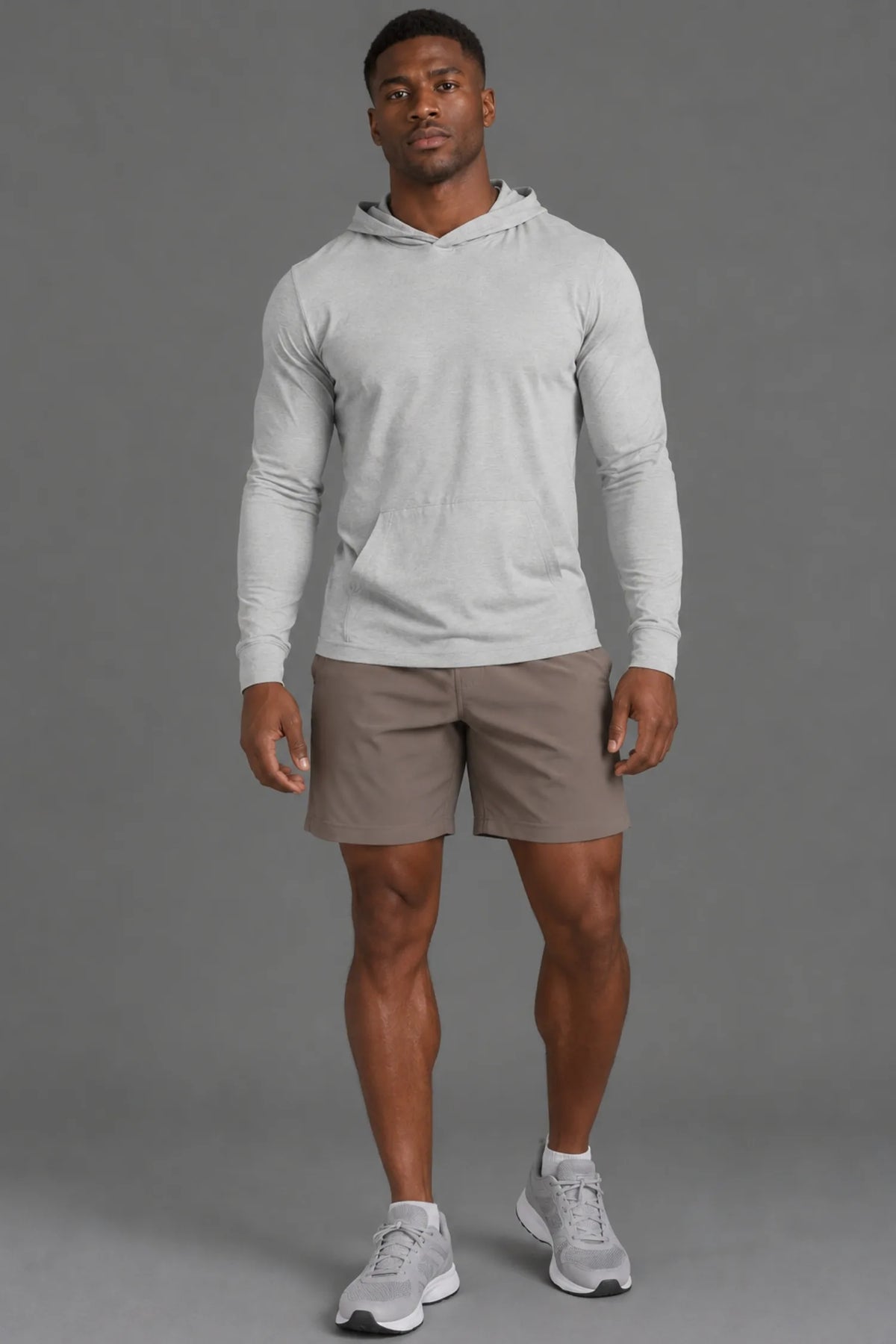 Black male model wearing a light gray performance hoodie with brown athletic shorts, ankle socks, and gray sneakers.