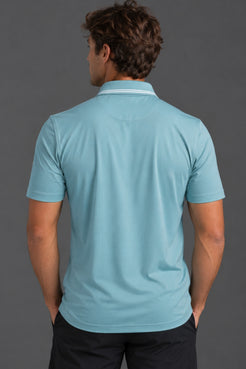 A man viewed from behind wearing a light blue short-sleeve polo shirt with a white stripe detail on the collar, paired with dark pants, against a solid dark gray background. || Underseas
