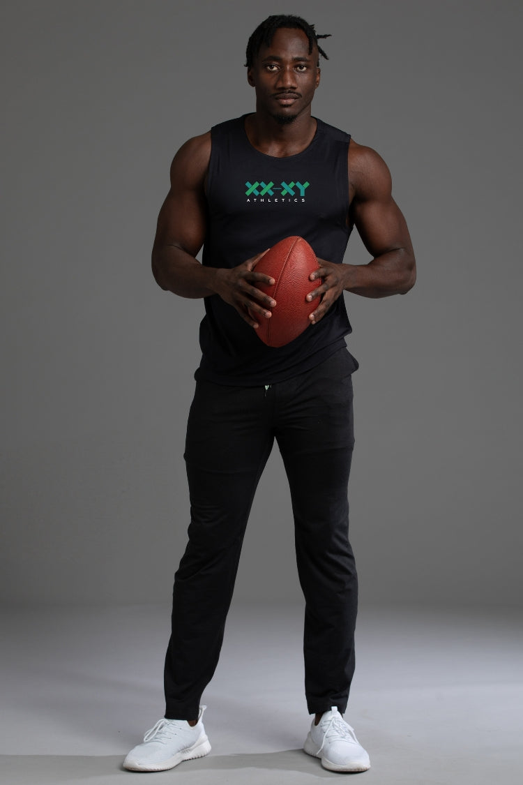 Man holding a football wearing a black tank top with a logo and black pants on a gray background || Black