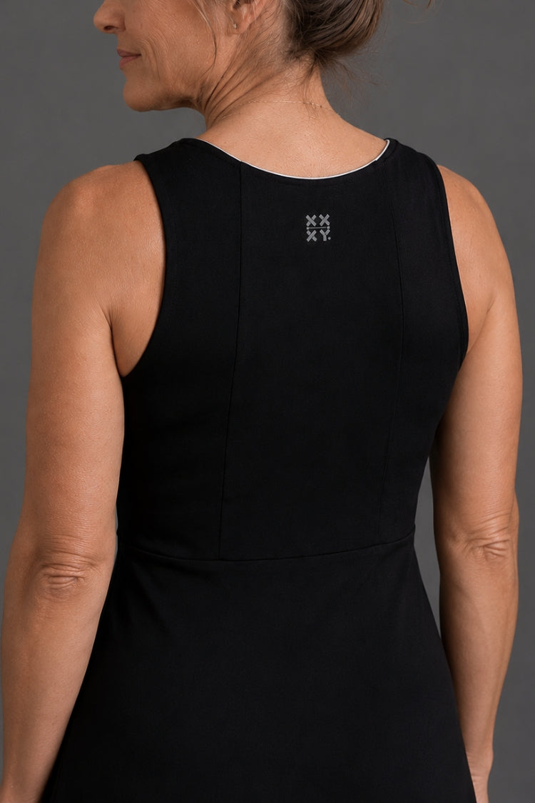 Person wearing a black sleeveless top with a small logo on a gray background || Black