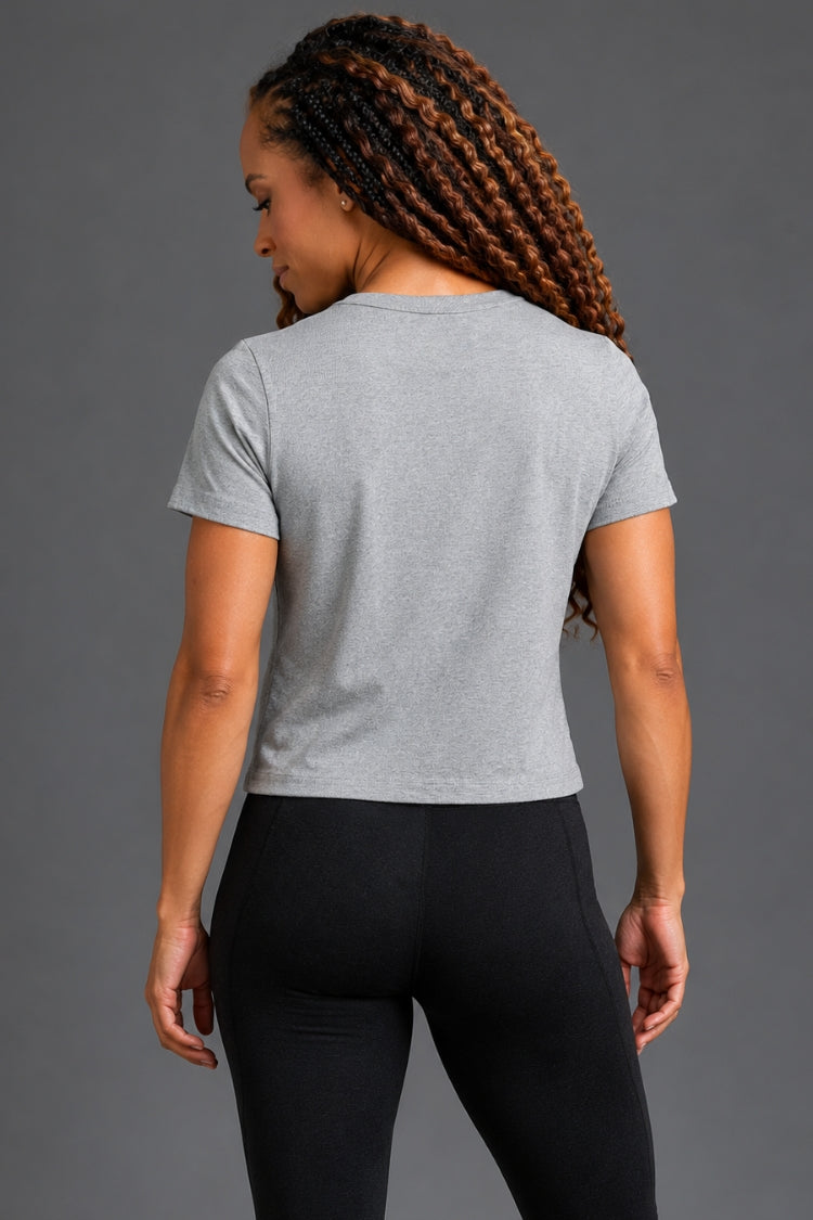 Woman wearing a gray t-shirt and black leggings against a gray background