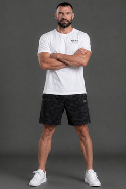 Man wearing a white t-shirt and black shorts with a brand logo, standing against a gray background || White