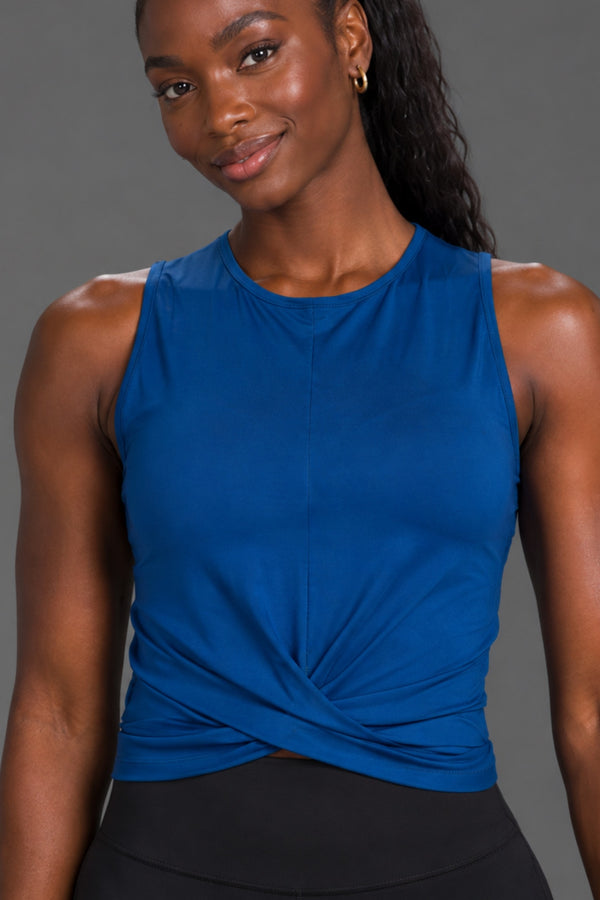 Black female model smiling in a blue twist-front athletic tank and black XX-XY Athletics leggings. || Navy