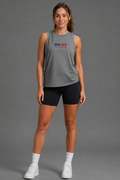 A woman modeling a heather gray sleeveless athletic tank top with a red and blue 'XX XV ATHLETICS' logo on the chest, paired with black athletic shorts, white socks, and white sneakers, against a solid gray studio background. || Dark Heather Gray
