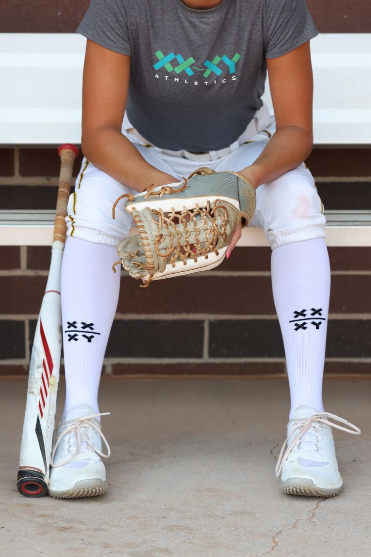 Person sitting on a bench wearing a gray 'XXXY Athletics' t-shirt, white pants || Black/White
