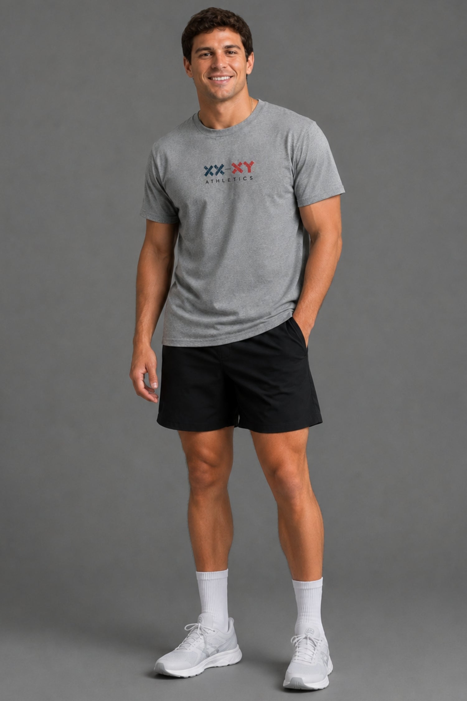 A man modeling a heather gray short-sleeve t-shirt with a 'XX-XY Athletics' logo on the chest, paired with black athletic shorts, white socks, and white sneakers, against a solid gray studio background.