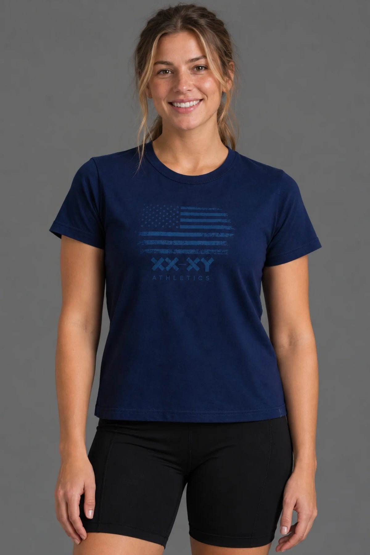 Female model smiling in a navy tonal American flag graphic tee with black bike shorts.