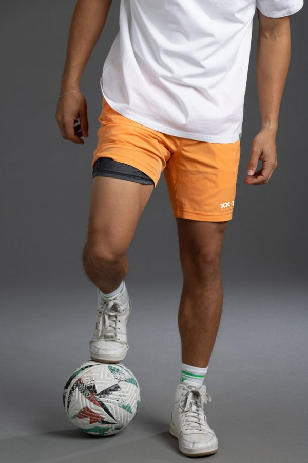 Person wearing orange shorts and white sneakers with a soccer ball on a gray background || Light Orange