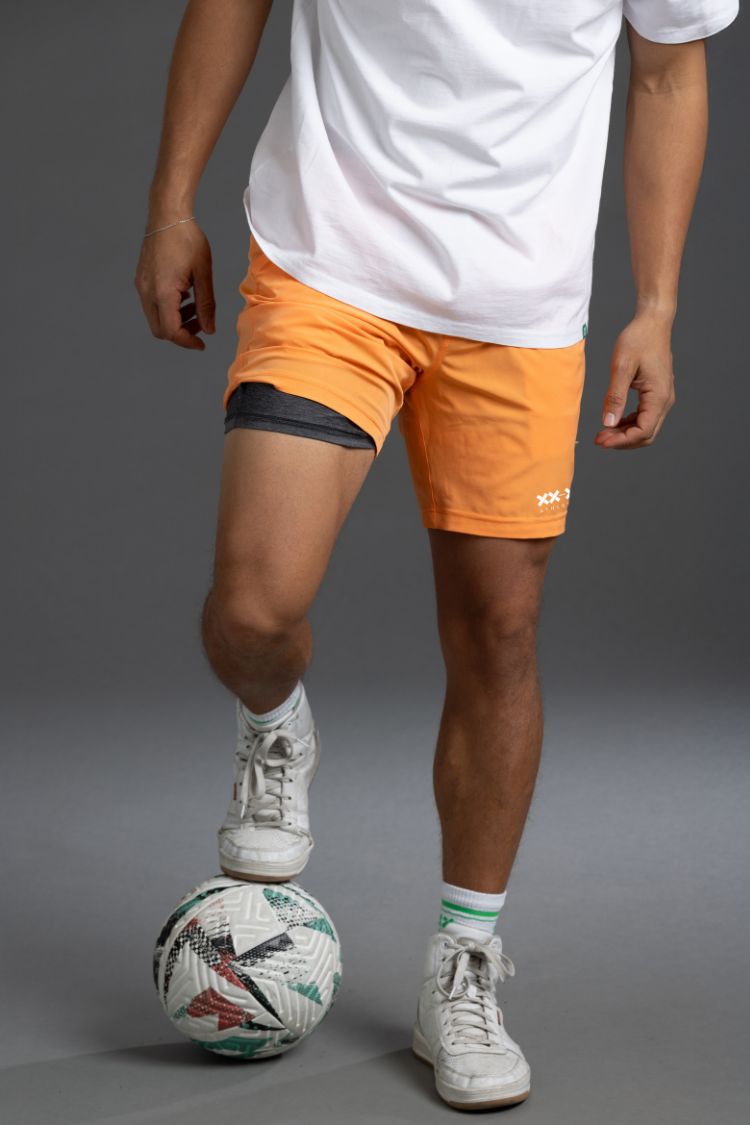 Person wearing orange shorts and white sneakers with a soccer ball on a gray background || Light Orange